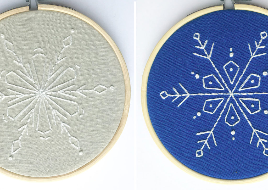Two DIY Christmas Ornament snowflake embroidery hoops. One snowflake has a blue background the other gray. Both have white stitching.