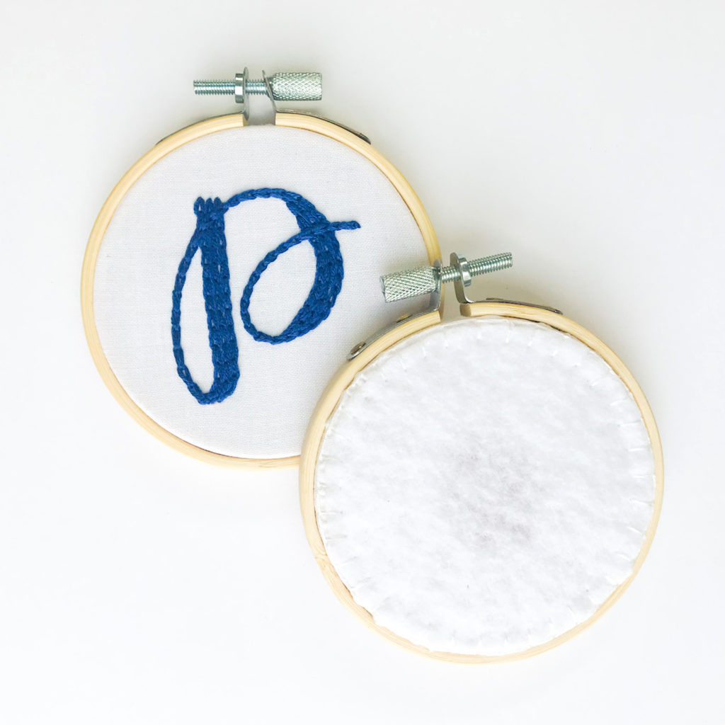 Front and back of Initial ornament hoop show side by side. Front has letter "P" and back is finished with white felt. 