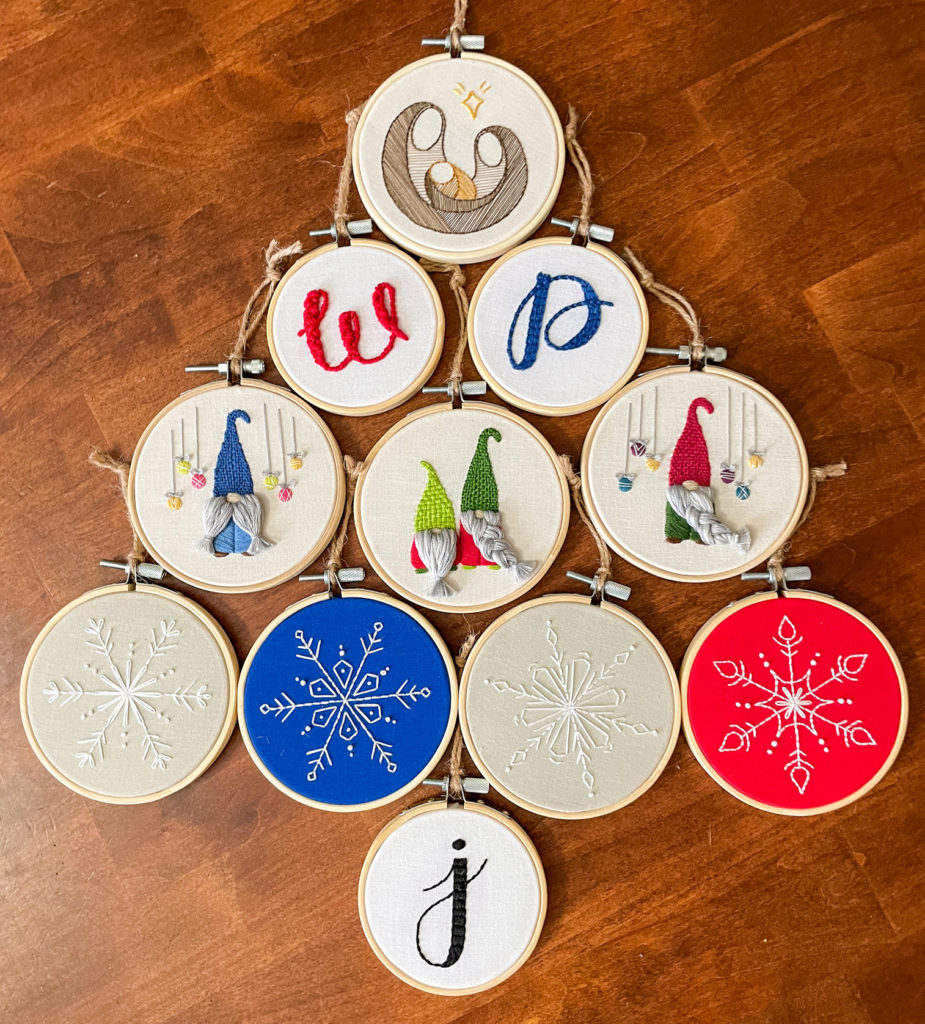 DIY Christmas ornament hoops arranged to look like a Christmas tree. Hoops include, initials, snowflakes, Gnomes, and a nativity scene. 
