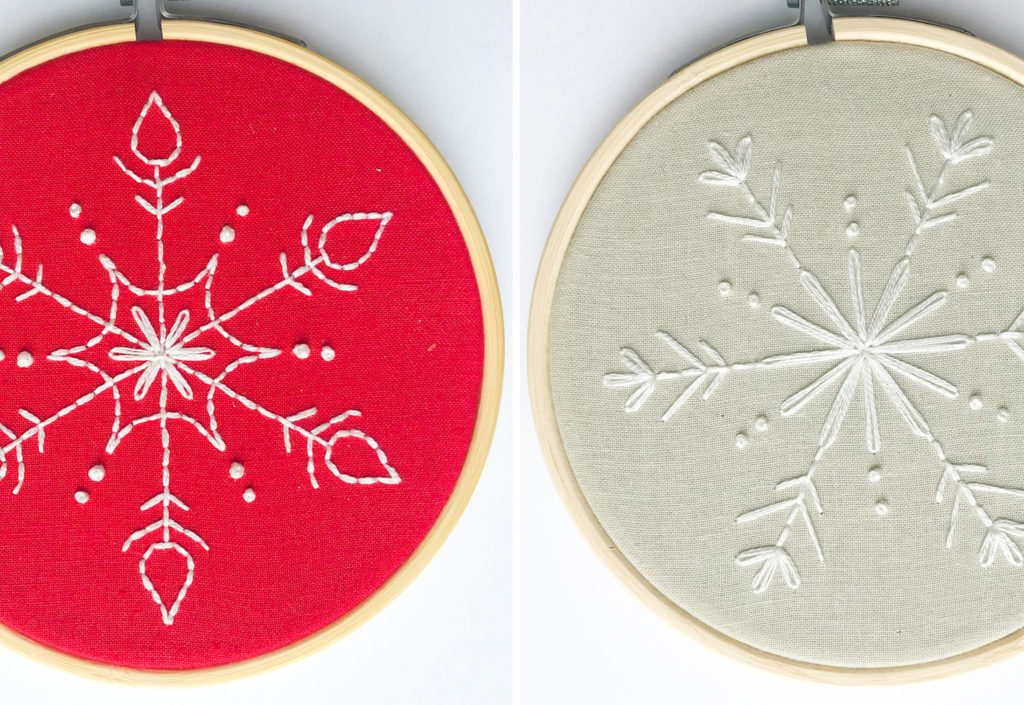 Two DIY Christmas Ornament snowflake embroidery hoops. One snowflake has a red background the other gray. Both have white stitching.