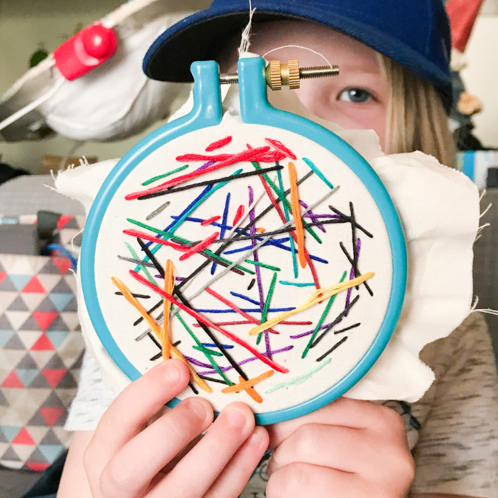 Picture of a small hoop with random lines of stitching one it being held by a child. 
