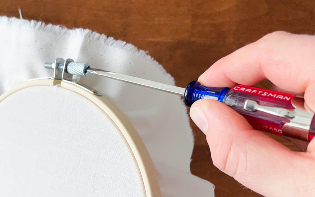 Images show a hand holding a screwdriver tightening the bolt on an embroidery hoop. 