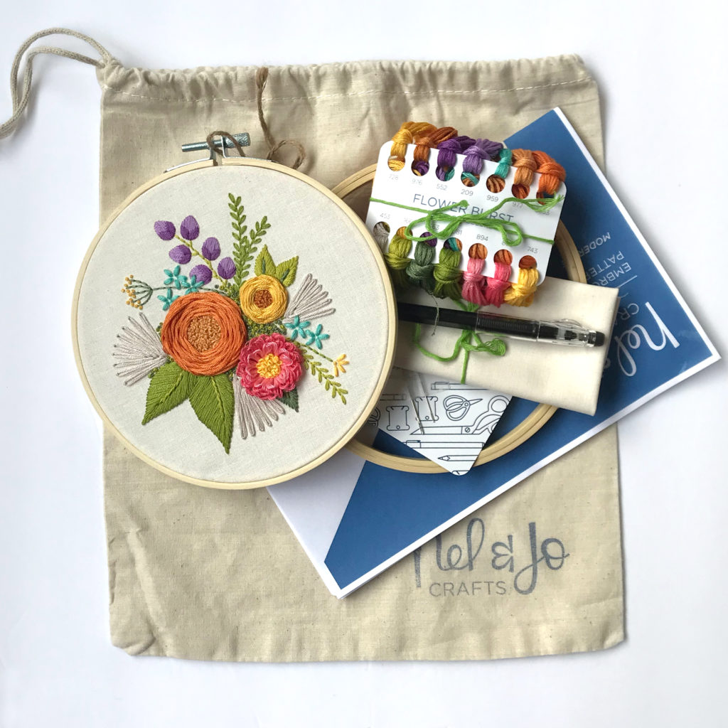 Picture of the flower burst embroidery hoop. Also shown are the supplies included in the kit, embroidery floss, fabric, tracing pen, needles, hoop, instructions and project bag.