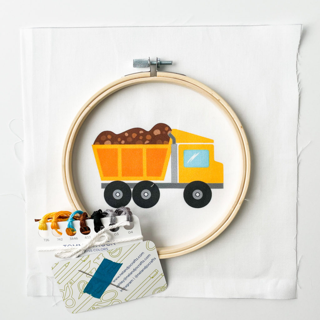 Image of a yellow dump truck printed on fabric with embroidery supplies around it.