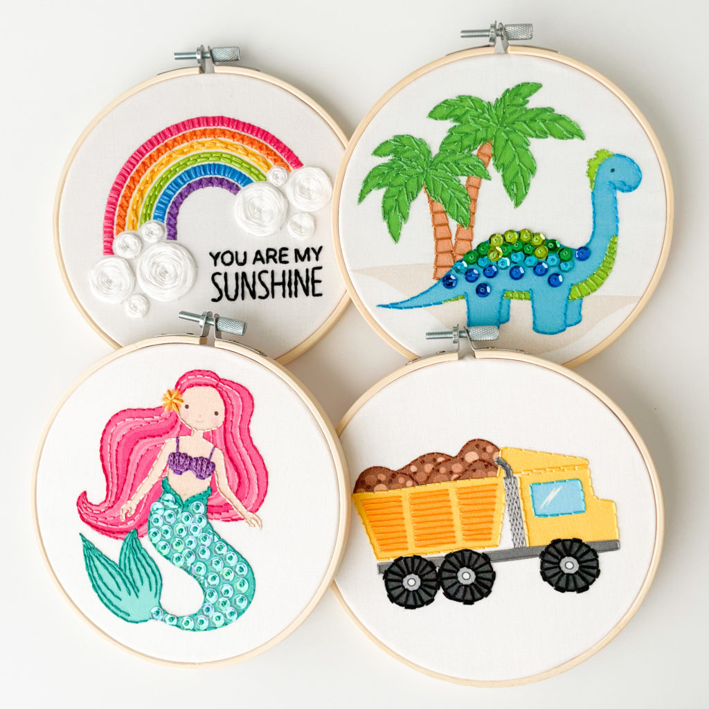 4 finished kid embroidery hoops. One Rainbow hoop, one dinosaur hoop, one mermaid hoop, and one dump truck hoop. 