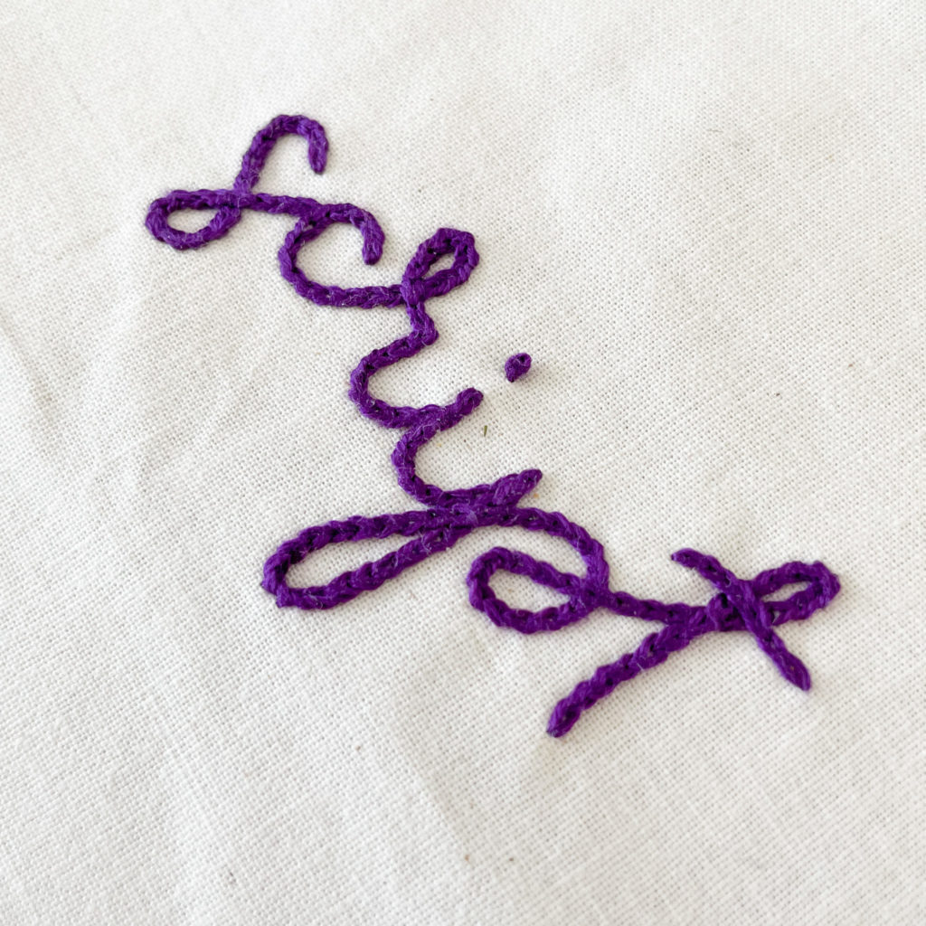 The word "script" stitched on fabric. Showing how to make embroidery lettering overlap.