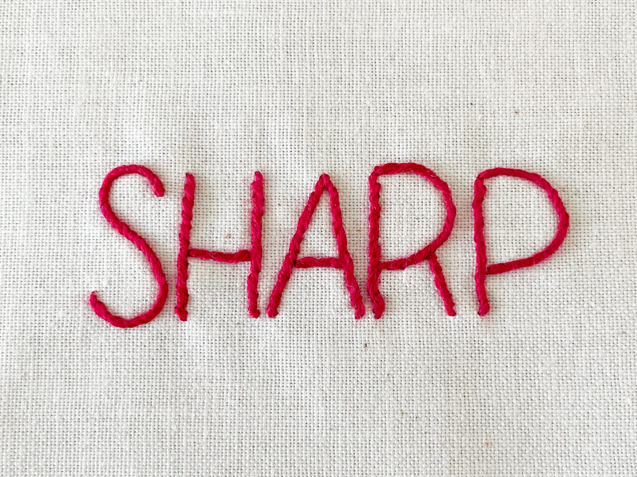 The word "sharp" stitched on fabric.