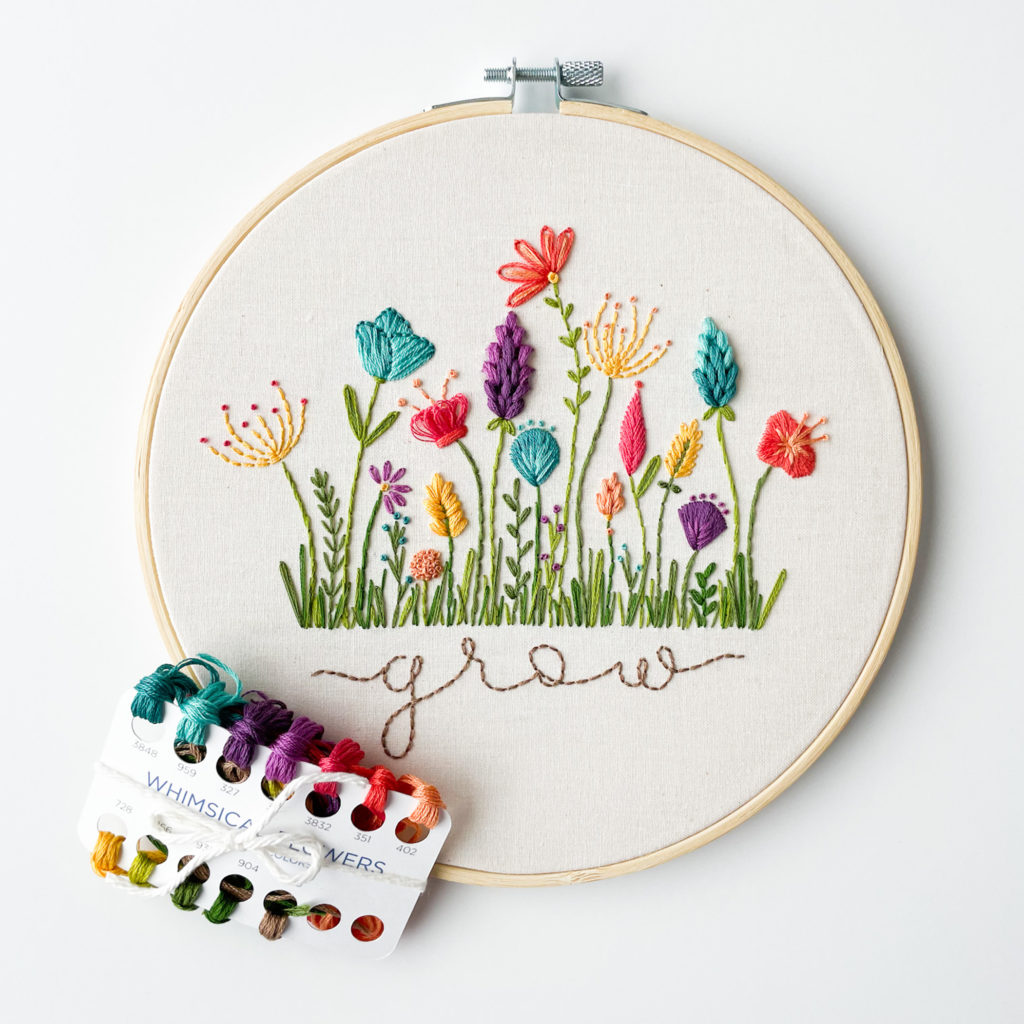 Image shows an embroidery hoop with a line of flowers stitched over the word "grow."
