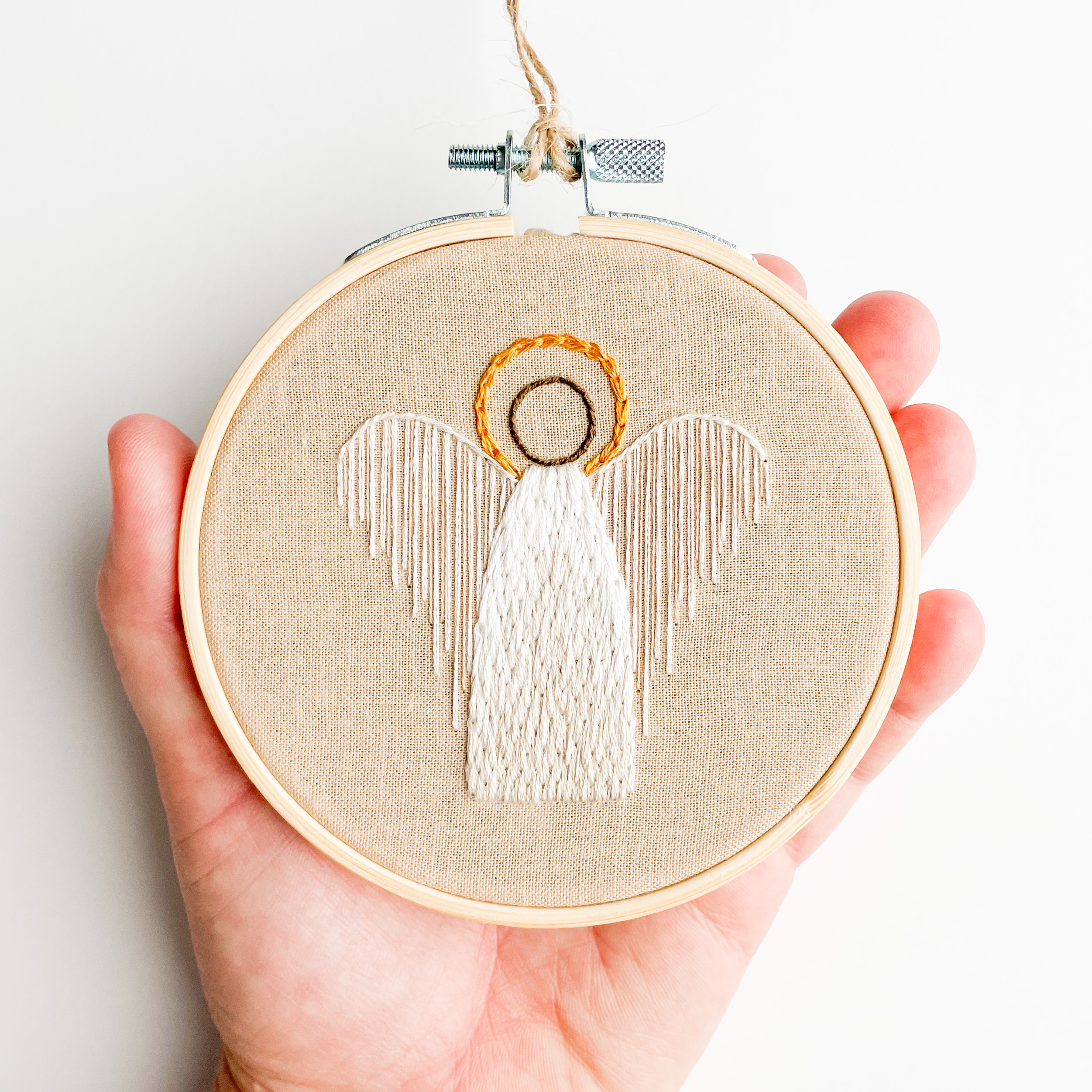 Image of a hand holding a small embroidery hoop with and image of an angel with a halo stitched on it.